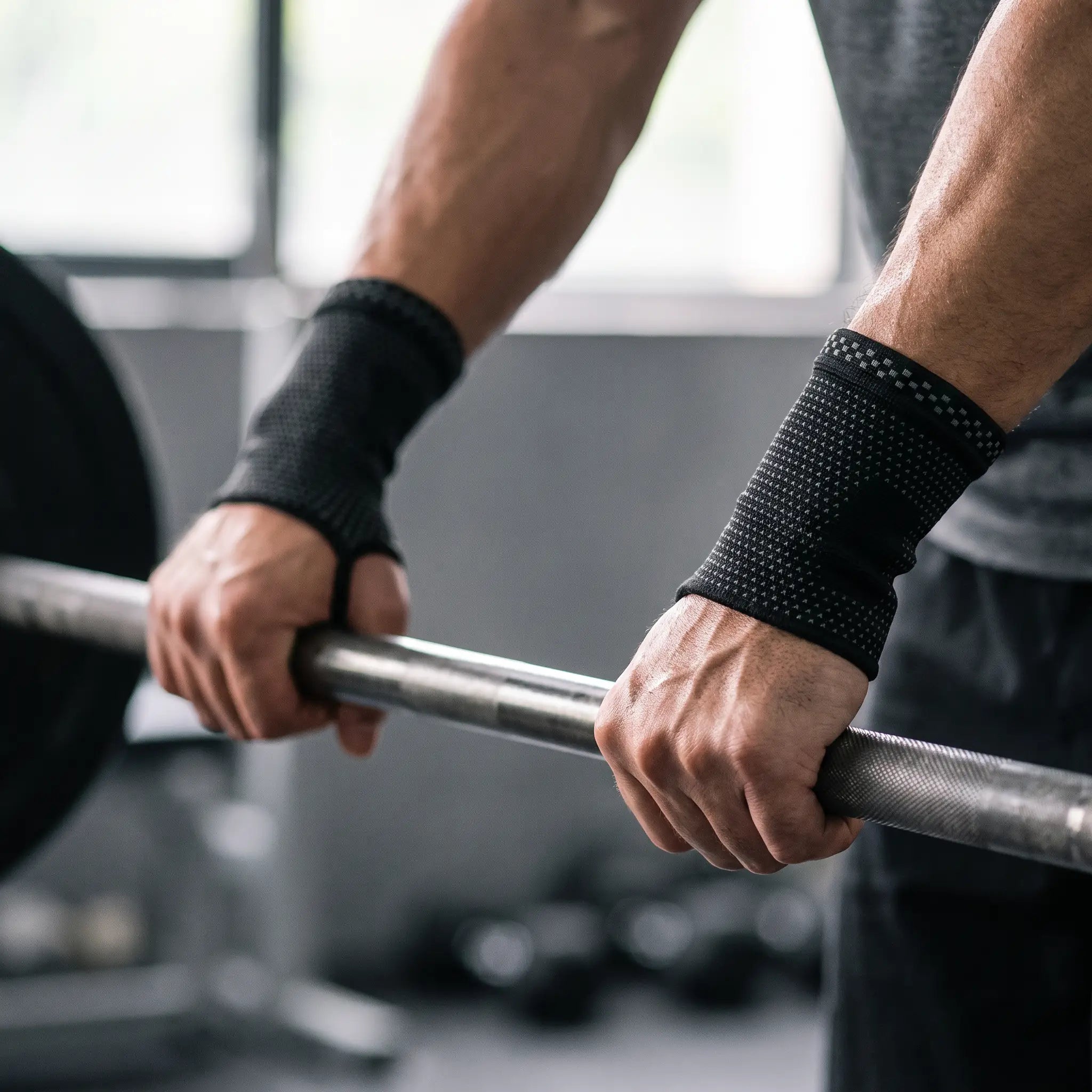 Mains sur une barre de musculation portant les manchons poignet et paume Flexnea